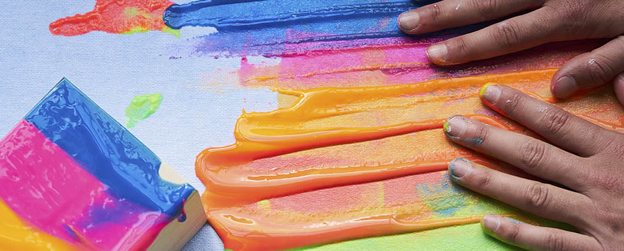 a child's hands spreading colorful finger paints on a countertop
